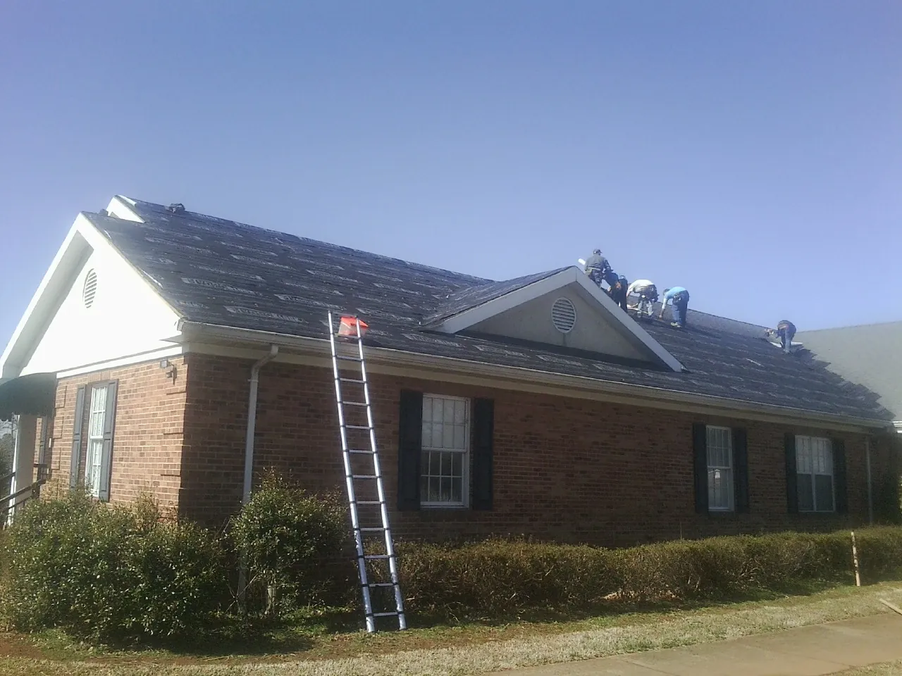 Crew tearing shingles off a brick ranch roof with a ladder set — Metal Roof Repair work by our crew in Summit Hill