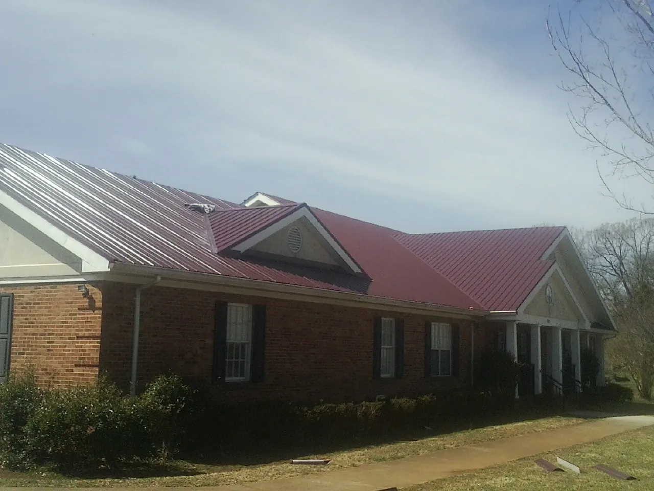 Red metal roof with gabled entries on a long brick building, from a Hail Damage Roof Repair job in Summit Hill