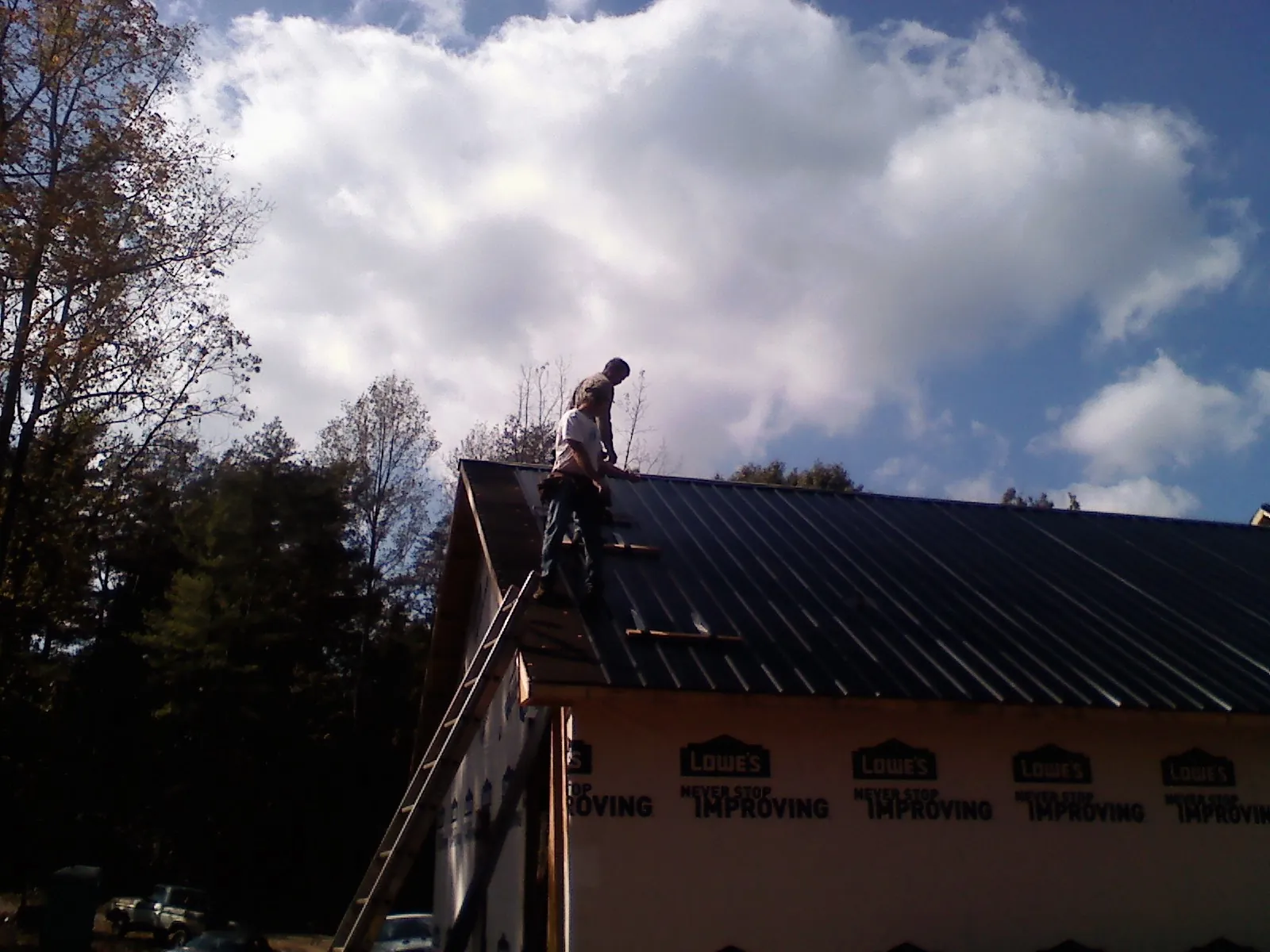 Roofer fastening dark metal panels high against a cloudy sky, from a Roof Inspection job in Summit Hill