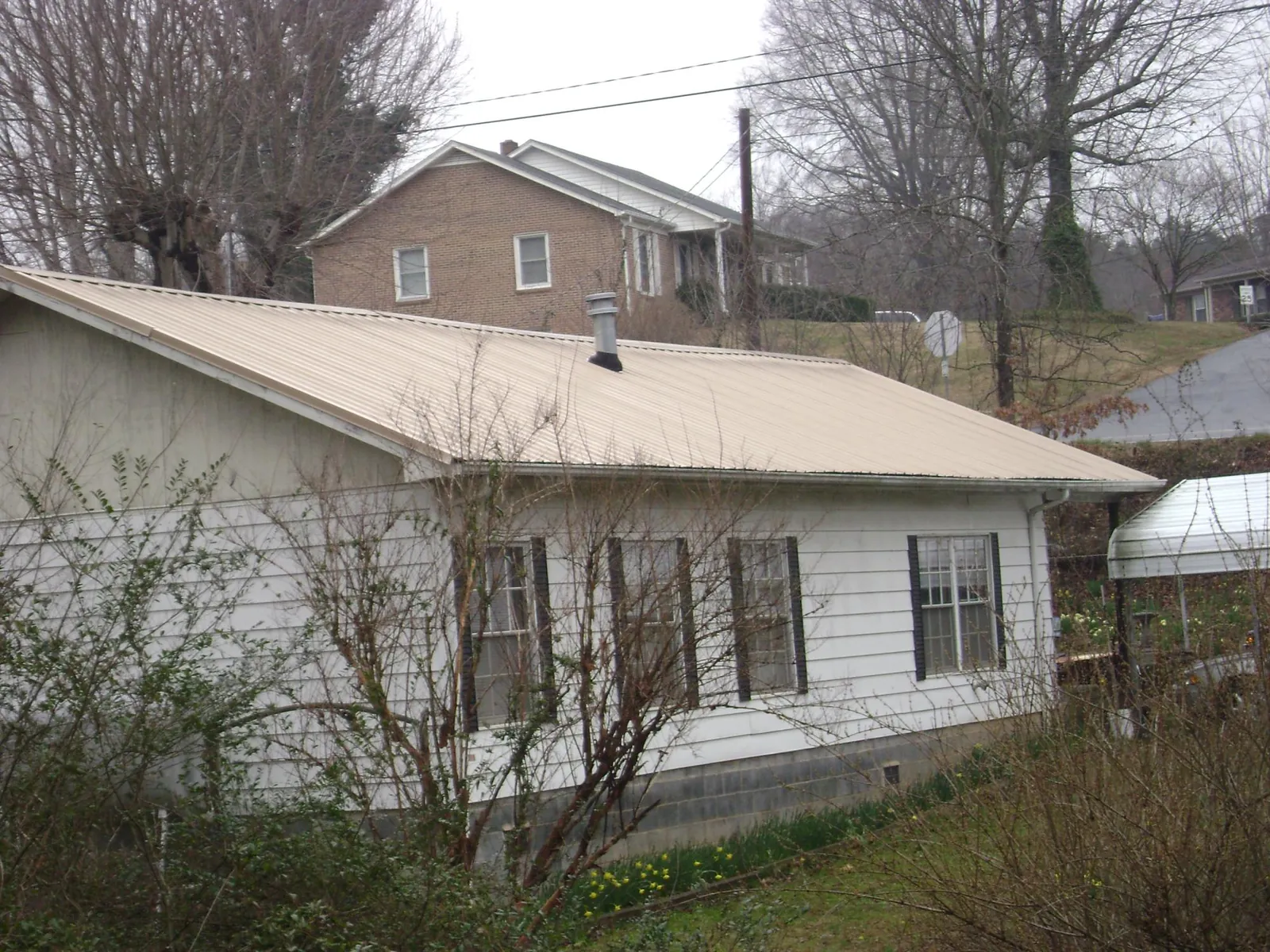 Tan metal roof on a white sided house set into a hillside — Commercial Roofing by Roofing Brothers in Summit Hill