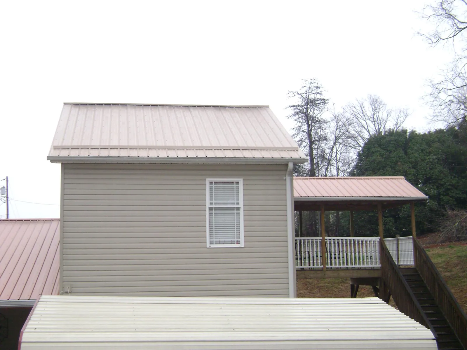 Tan metal roofs on a two story addition and attached porch, from a Roof Replacement job in Summit Hill